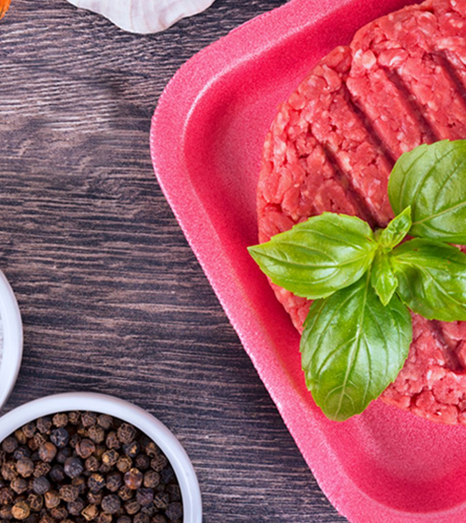 A red tray with ground meat and basil leaves.